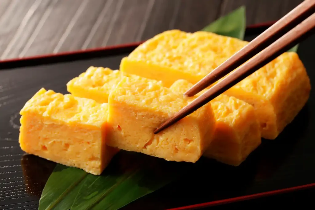 一款卷得完美、质地如天鹅绒般柔滑的日式卷蛋(dashimaki tamago),被切成厚实而优雅的片